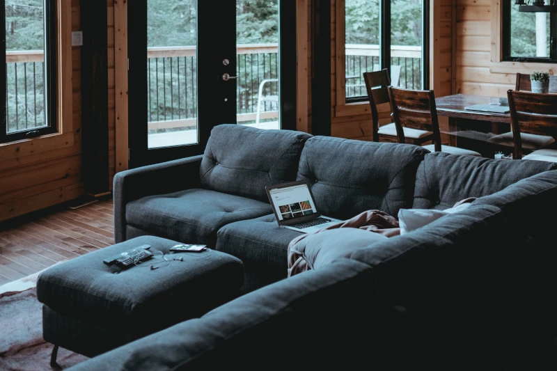 Gemütliches Wohnzimmer mit Sofa, Laptop und Blick in den Wald durch Fenster